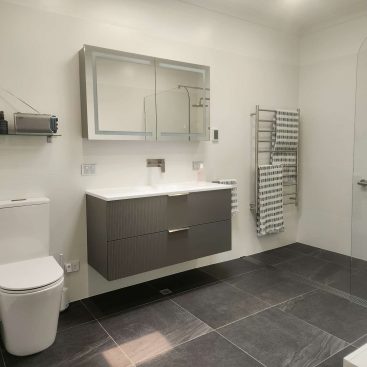 Open plan bathroom featuring floating vanity, toilet and a glass walled shower.