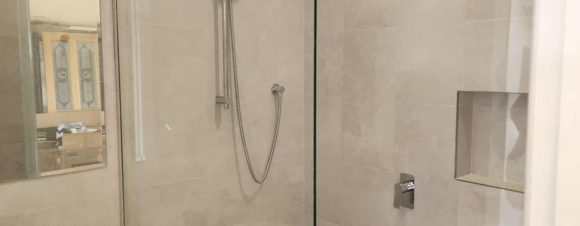 Glass shower screen, white vanity on wooden drawers in a garage converted to a bathroom.